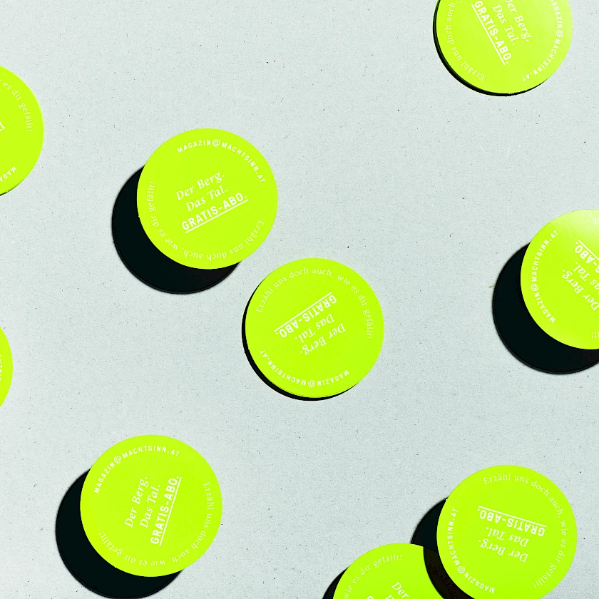 Viele Sticker des Magazins Berg &amp; Tal des TVB Grimming auf grauem Hintergrund.